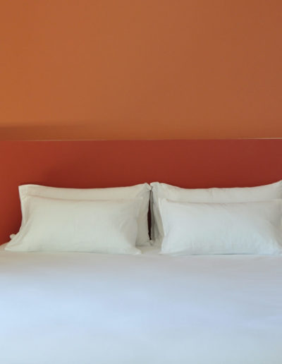 Lit double avec mur orange en tête de lit, sete hebergement, Les Clés Secrètes.
